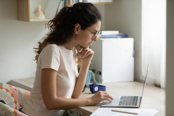 istock Serious woman wearing glasses using laptop, working on project 1295072572