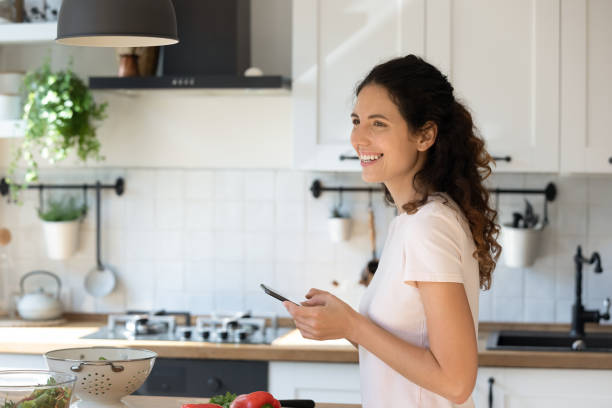 istock Overjoyed attractive woman using phone, standing in modern kitchen, cooking 1295072651