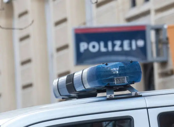 Blue light on the roof of a police car, police station (Polizei) sign blurred in the background