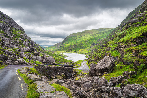 Narrow winding road and stone bridge with a view on Gap of Dunloe valley and lake in Black Valley, Ring of Kerry, County Kerry, Ireland