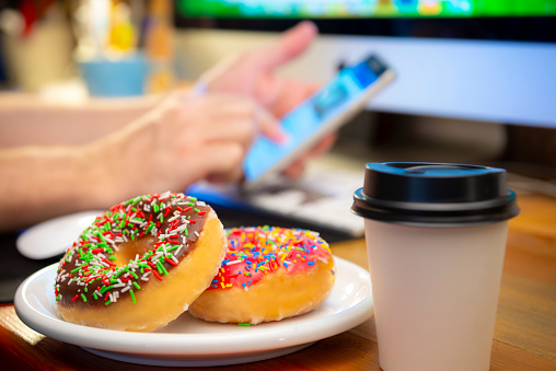 Fresh Donuts waiting to be eaten. People using computer as background.