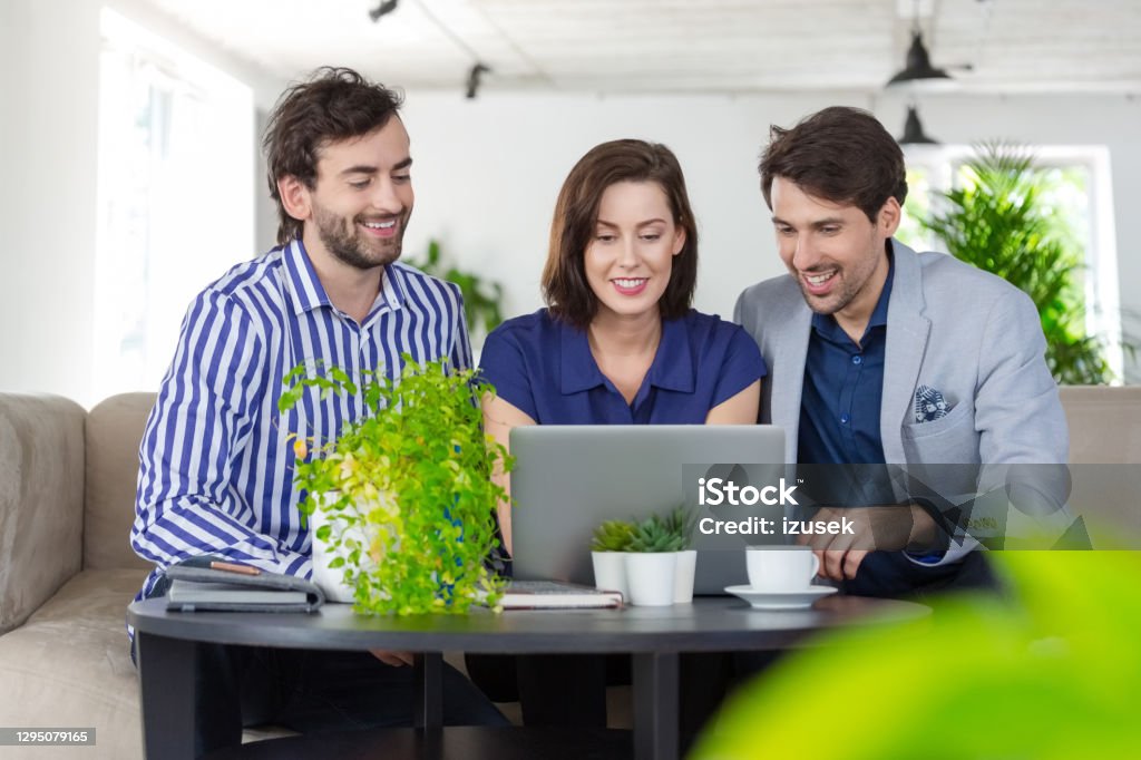 Business people working in a green office Mid adult women and men sitting on sofa in the creative eco-friendly workplace, working together over laptop. Business Person Stock Photo