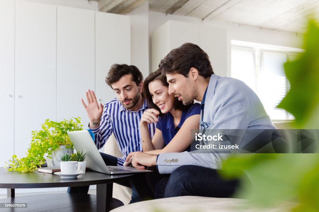 Business team during video call in a green office Mid adult women and men sitting on sofa in the creative eco-friendly workplace, using laptop during video conference. 30-39 Years Stock Photo