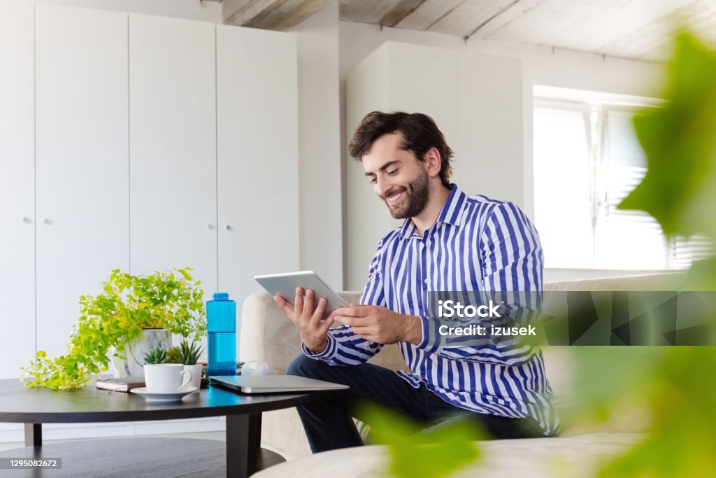 Man working in the eco-friendly green office Mid adult men wearing striped shirt sitting on sofa in the creative workplace and using digital tablet. Working Stock Photo