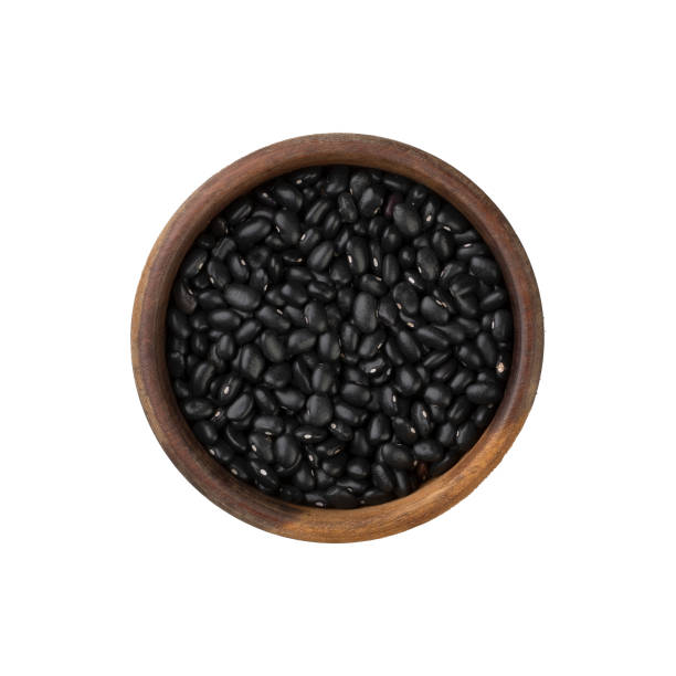 istock Raw black beans on a wooden bowl isolated over white background 1295087500