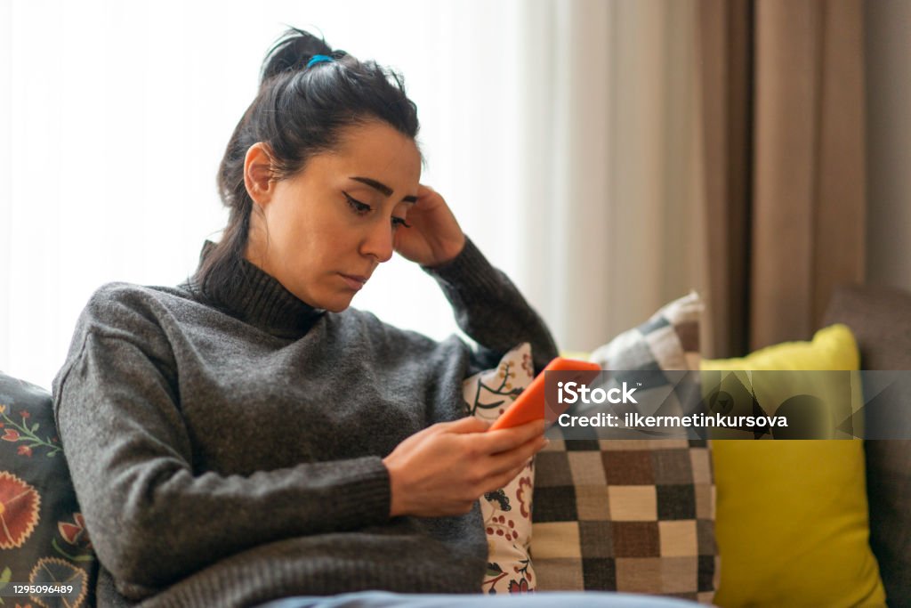 Woman looking at mobile phone screen at home. Woman sitting on a sofa and looking at mobile phone screen at home. Women Stock Photo