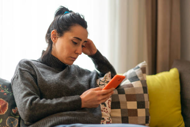 Woman looking at mobile phone screen at home. Woman sitting on a sofa and looking at mobile phone screen at home. waiting telephone on the phone frustration stock pictures, royalty-free photos & images