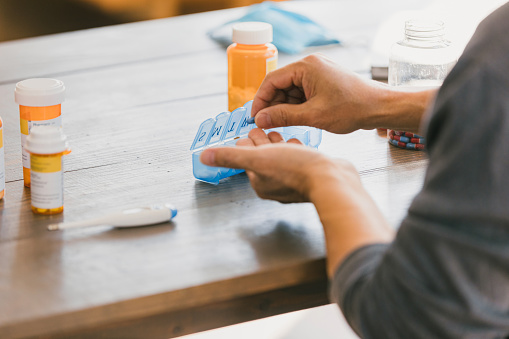 An unrecognizable man uses a pill organizer to sort out his man prescription medications.