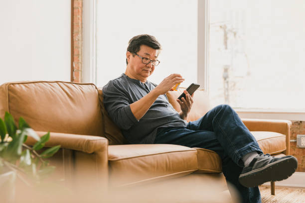 hombre de la tercera edad utiliza aplicación móvil de farmacia para rellenar la receta - sofa men adult aging process fotografías e imágenes de stock