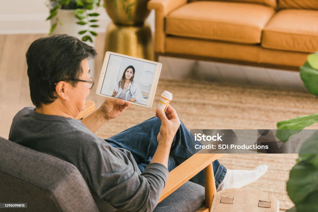Man talks with doctor during telemedicine appointment During a virtual appointment, a senior man discusses his current medications with a female doctor. Telemedicine Stock Photo