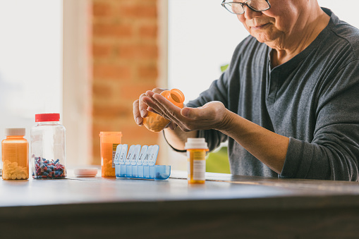 A retired senior man pours pills from a pill bottle into his hand as he organizes the medication into a weekly pill organizer.
