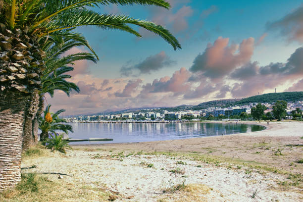 istock Greek cityscape with it's reflection on water and palm tree against dramatic clouds and mountains 1295103673