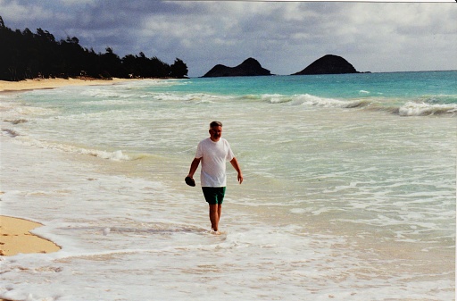 A mature man wading by an Oahu beach on the North Shore in Hawaii. An island in view from the sandy beach coastline. Copy Space.