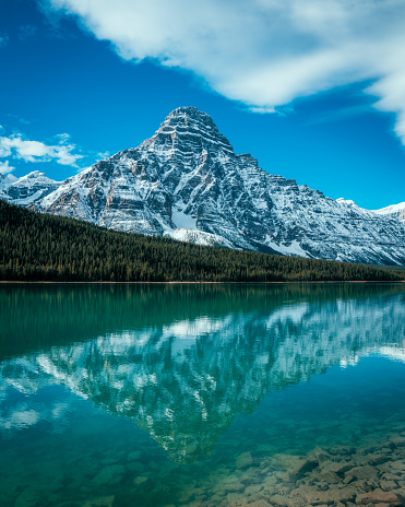 A summer reflection at Waterfowl Lakes with a mountain range in the back and contrasting clouds in the sky.