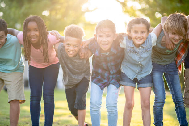 Summer camp friends are the best friends! A beautiful multi ethnic group of elementary age children huddled together for a photo. They are embracing each other while smiling and laughing. 12 13 years stock pictures, royalty-free photos & images