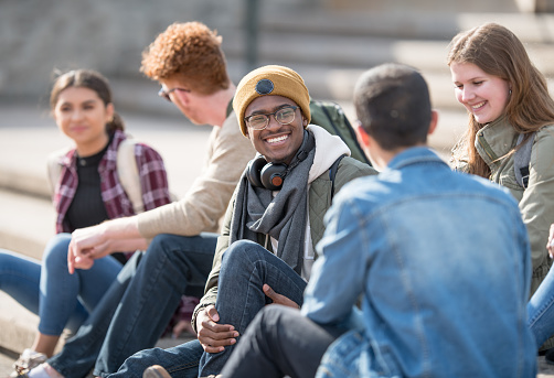 A multi ethnic group of university students are hanging out outdoors on campus.