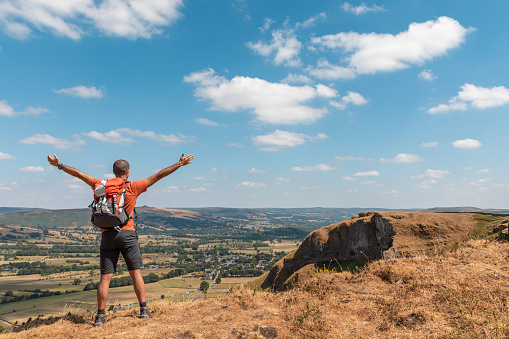 Man with raised arms on top of cliffs in Peak District