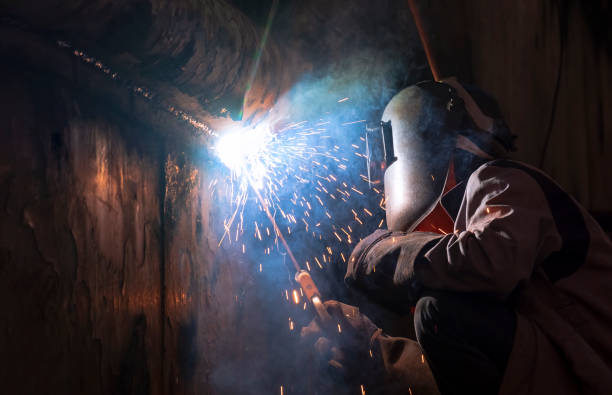 welder with safety equipment using arc welding machine to welding metal wall of the old vessel at shipyard in evening time - employment issues flash imagens e fotografias de stock