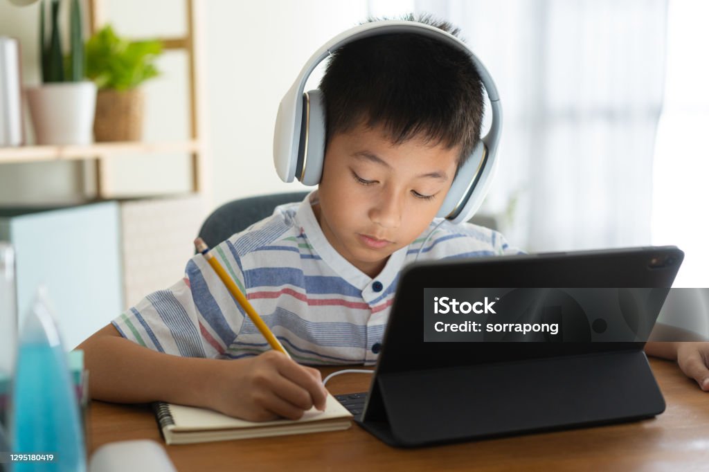 Asian boy learning online via internet with a tutor on a tablet digital with headphone, Asia child is studying while sitting in the living room at home. Concept of online learning at home Child Stock Photo