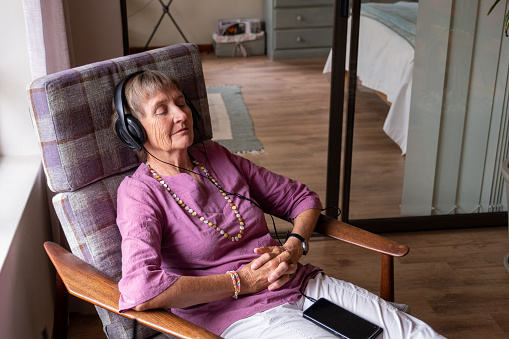 An elderly woman relaxes, she has earphones on and listens to some music. Senior woman enjoying her retirement years.