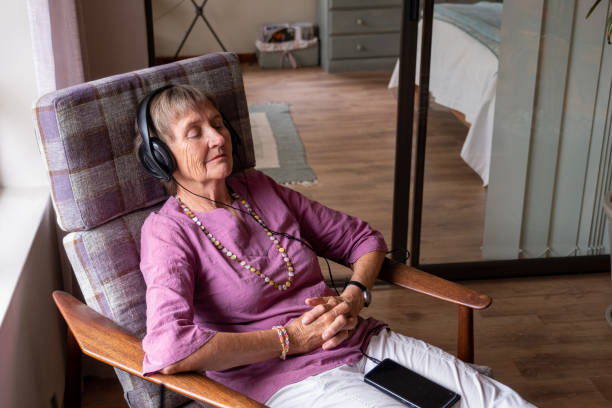 Senior woman sits and relaxes with music in her ears An elderly woman relaxes, she has earphones on and listens to some music. Senior woman enjoying her retirement years. audio book stock pictures, royalty-free photos & images