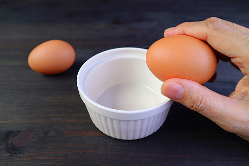 Man's hand holding an egg to crack into a bowl for cooking