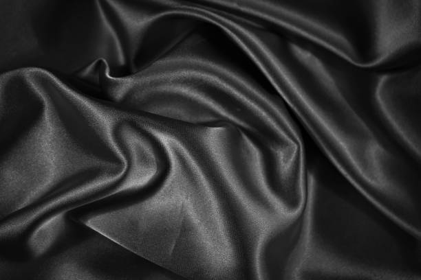 istock Black shiny fabric background. Dark abstract background. Wavy soft folds on the fabric. 1295200524
