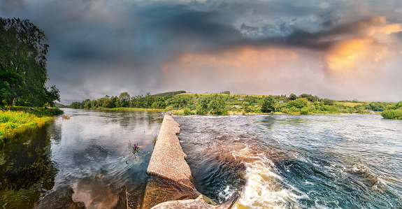 Panoramic view of concrete dam on river Lee in Ballincollig Regional park in summer on cloudy day. Ireland.