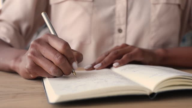 African woman holding pen writes notes in diary, closeup view