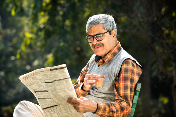 istock Senior man drinking tea and reading newspaper at park bench 1295218554