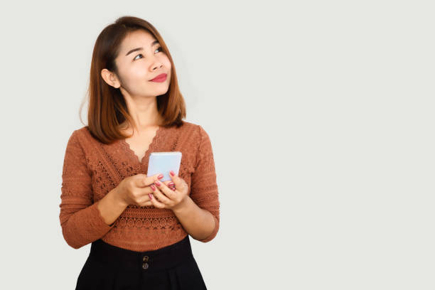 istock happy Asian woman hand using smart phone standing looking up day dreaming 1295219006
