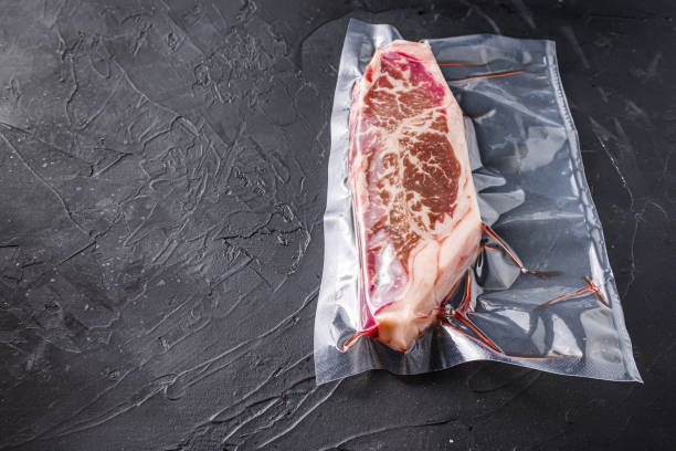 istock Top blade steak,  vacuum packed organic beef for sous vide cooking  on black textured background, side view with space for text. 1295220585