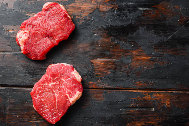 istock Raw rumpsteaks over dark old wooden background, above view with space for text. 1295222307