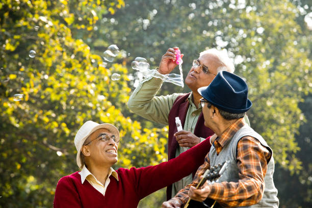 istock Three senior men playing guitar and blowing bubbles at park 1295223114