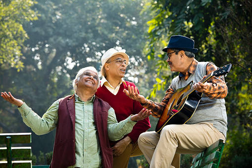 Three carefree senior male friends playing guitar and having fun at park