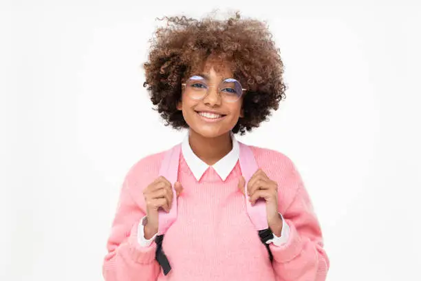 Photo of Studio portrait of pretty smiling african american teen girl, high school or college student with curly afro hair and pink backpack isolated on gray background