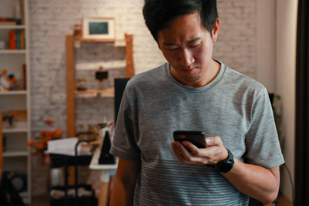 istock Yong Asian man using a mobile phone with frowning and worrying face expression with copy space 1295248100