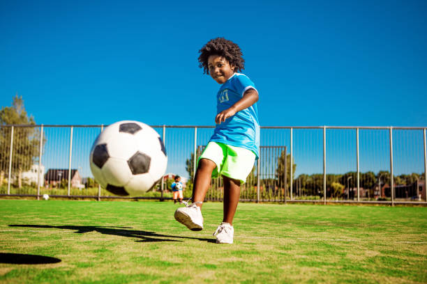 Beautiful young black boy training on the football pitch A young black boy child playing soccer on a neighbourhood football pitch on a beautiful sunny day in the Netherlands messing about stock pictures, royalty-free photos & images