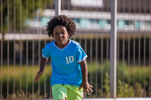 A young black boy child playing soccer on a neighbourhood football pitch on a beautiful sunny day in the Netherlands