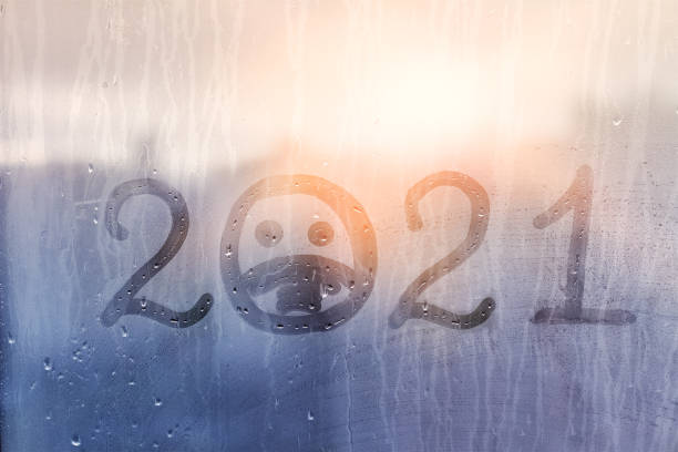 istock hahdmade painted numbers 2021 with sad face in protective medical mask on splashed by rain foggy glass on blue window, concept photo self-isolation, coronavirus, covid - 19 1295250929