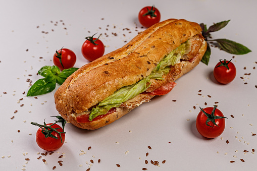 Appetizing baguette with chicken, tomatoes, cheese and ice salad. Snack or lunch. Homemade food. Close up