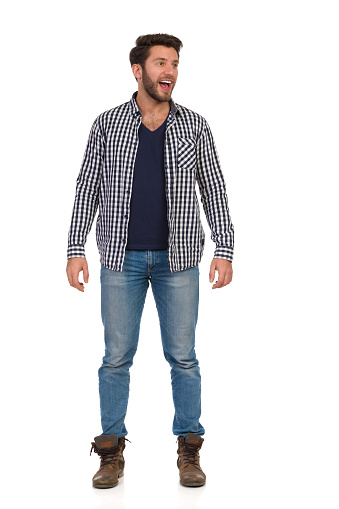 Happy casual man in unbuttoned lumberjack shirt is standing, looking away and shouting. Front view. Full length studio shot isolated on white.