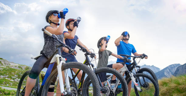 Family drinking water from water bottles while taking break during cycling trip in the mountains.