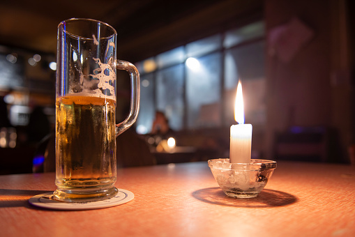 A beer and a candle over a wood table at night
