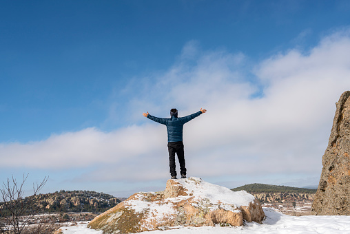 Hiker man standing on top of the hill covered with snow, with arms raised celebrating his success