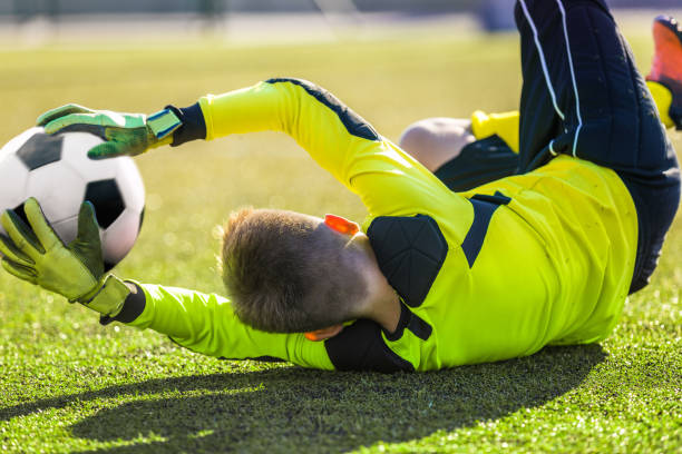 fußball goalie catching ball. young boy goalkkeeper retten ziel. akrobatische fußball-torwart speichern. fußballer in einem tor an einem sonnigen sommertag. soccer goalie training unit - ball halten stock-fotos und bilder