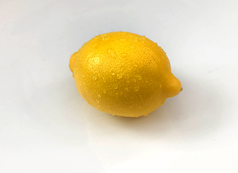 Single lemon against a white background with water droplets on the surface