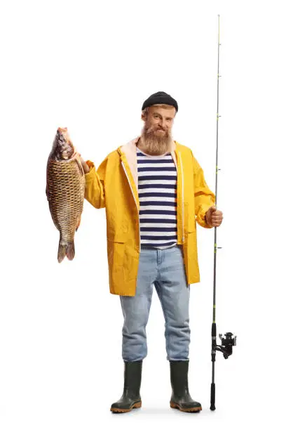 Full length portrait of a fisherman holding a fishing rod and a carp fish isolated on white background