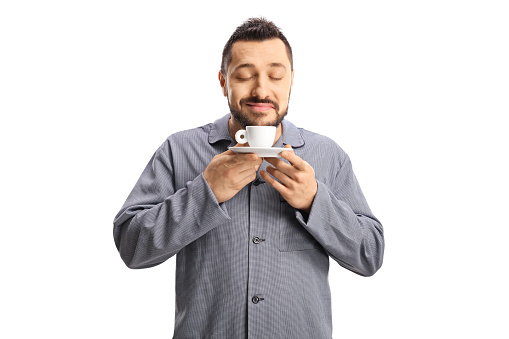 Man in pajamas smelling a cup of espresso coffee isolated on white background