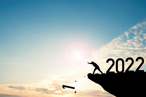 Man push number one down the cliff where has the number 2022 with blue sky and sunrise. It is symbol of starting and welcome happy new year 2022.